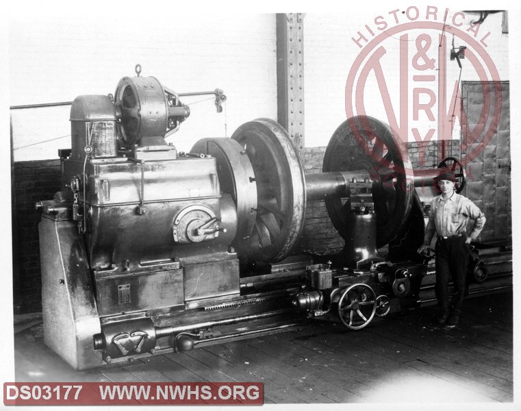 Man with large lathe who appears to be turning a locomotive axle.
